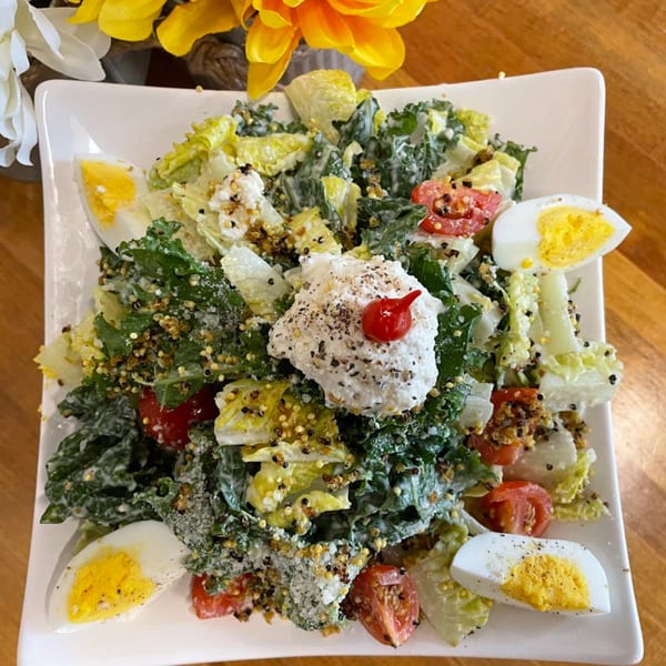 A vibrant salad with mixed greens, cherry tomatoes, quinoa, hard-boiled eggs, and a dollop of cheese.
