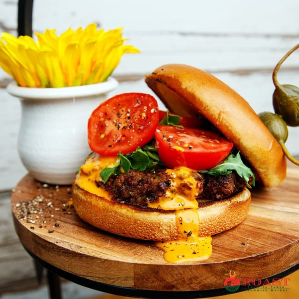 Roast's juicy cheeseburger with melted cheddar, fresh tomatoes, and arugula, served on a wooden board.