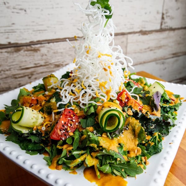 Roast's vibrant salad with greens, tomatoes, cucumber, and crispy noodles on a white plate.