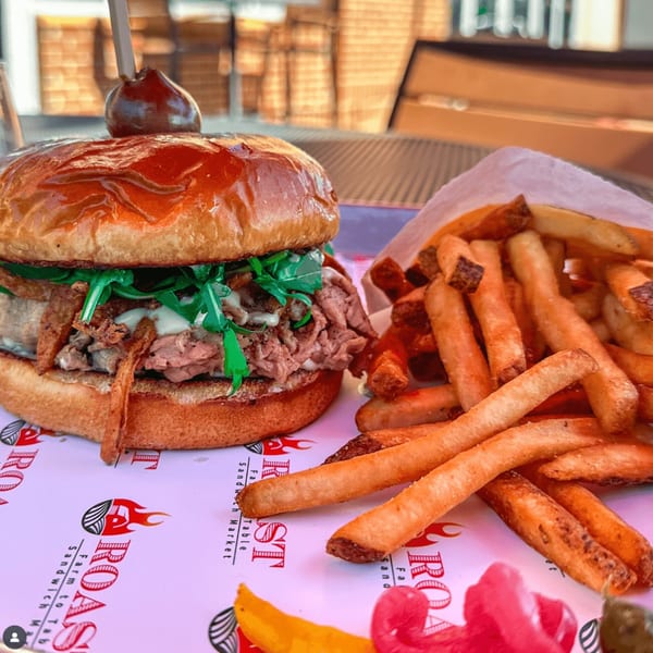 Roast's beef sandwich with arugula and sauce, served with a side of golden fries.