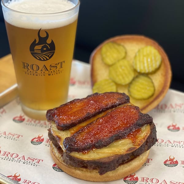 Roast's burger with bacon and cheese, a side of pickles, and a glass of beer.