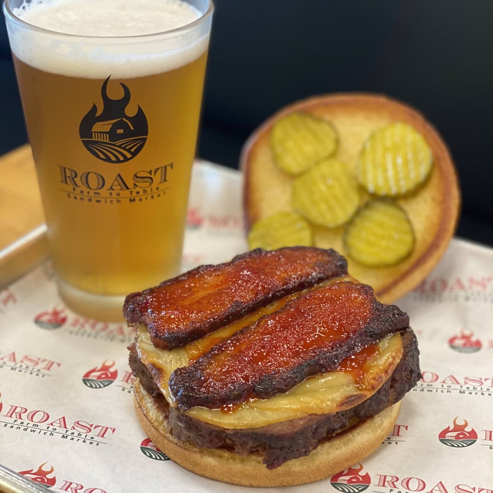 Roast's burger with bacon and cheese, a side of pickles, and a glass of beer.