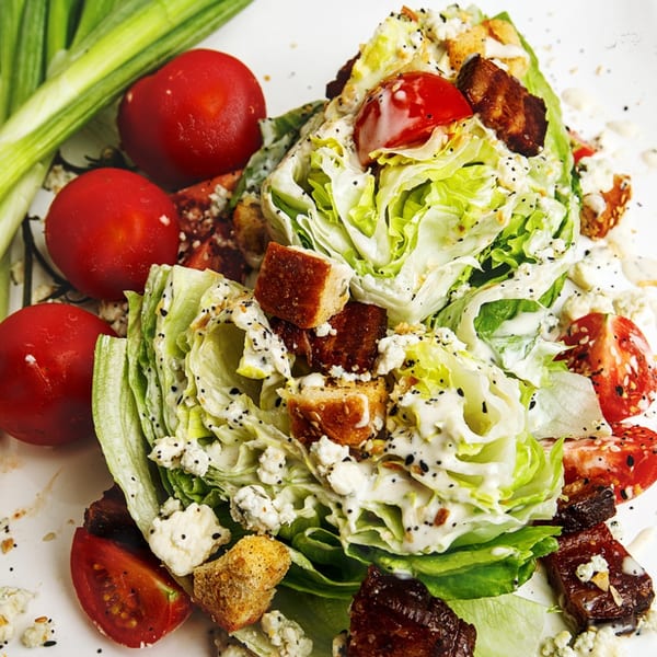 A wedge salad with lettuce, tomatoes, bacon, croutons, and blue cheese dressing.